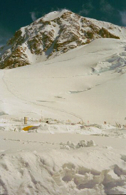 The steep rock wall of the West Buttress Direct route looming over the snowy 11K foot camp.